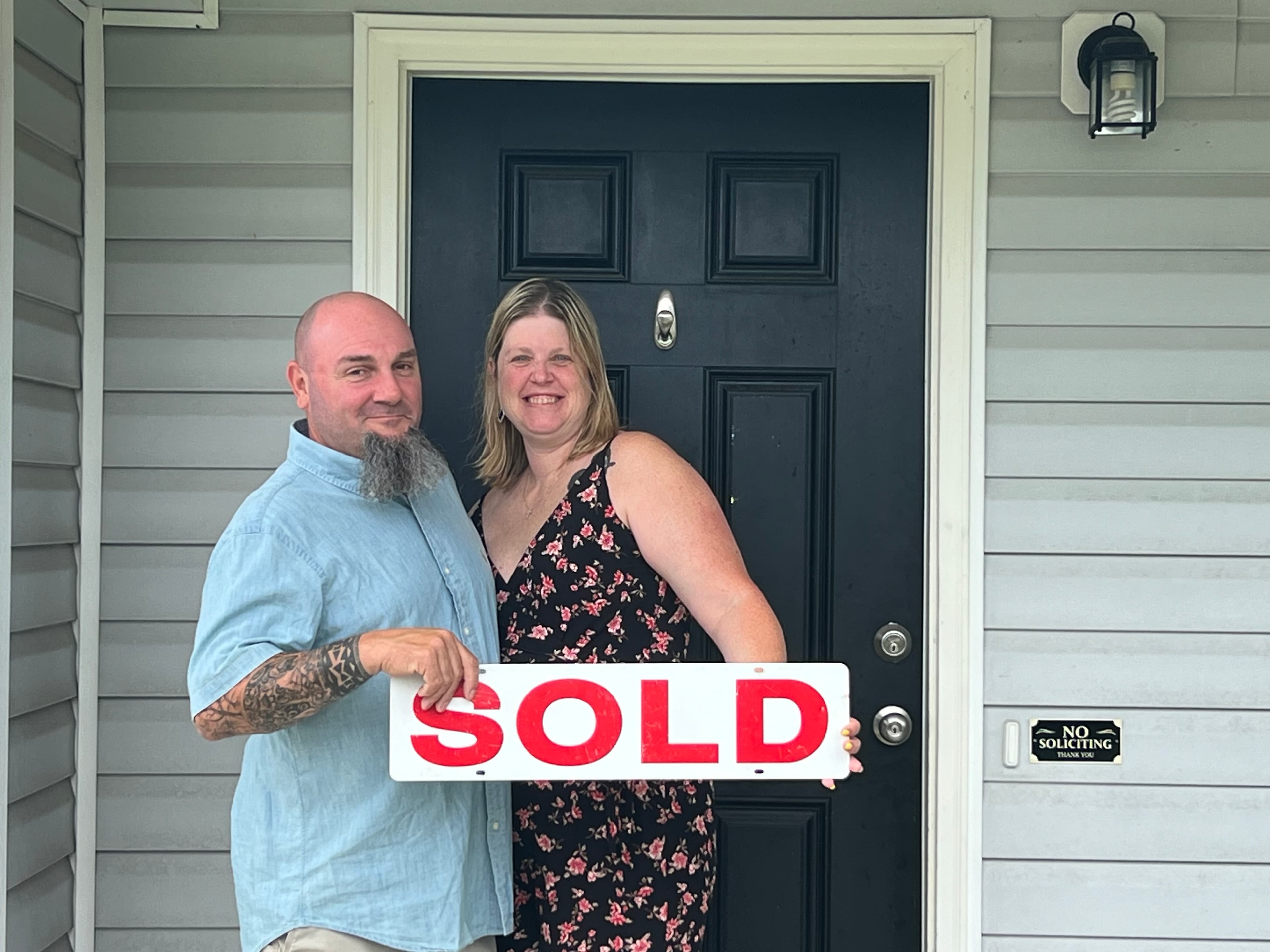 Couple holding SOLD sign at their new home