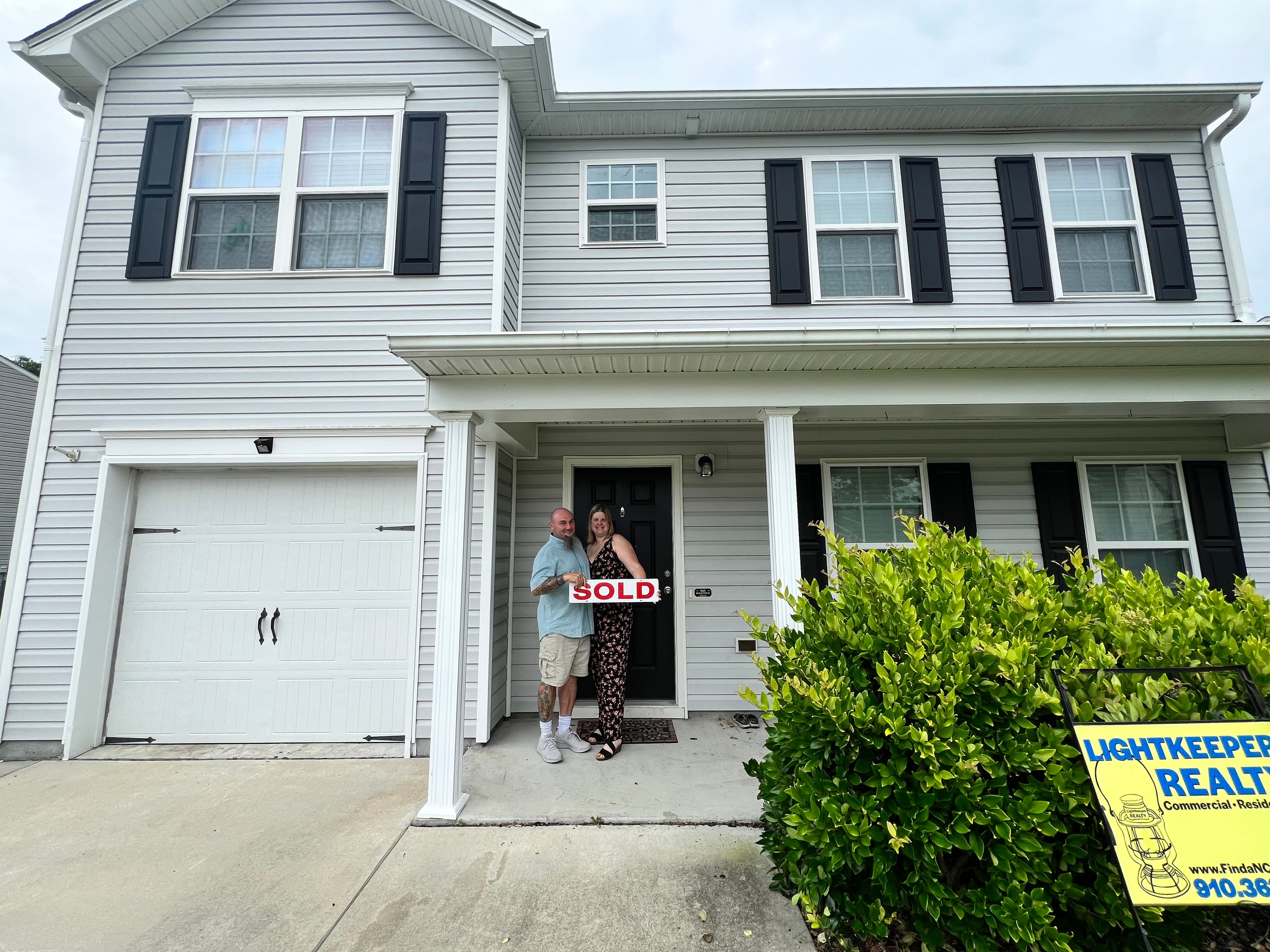 Happy couple at their sold home with Lightkeeper Realty sign